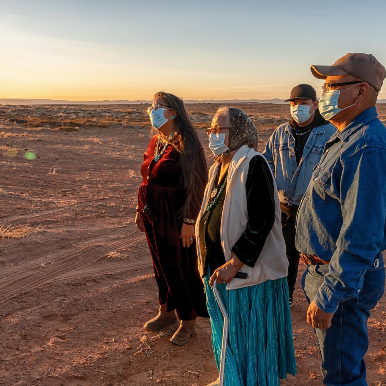 A Native American family is seen looking out at the sunset wearing masks.