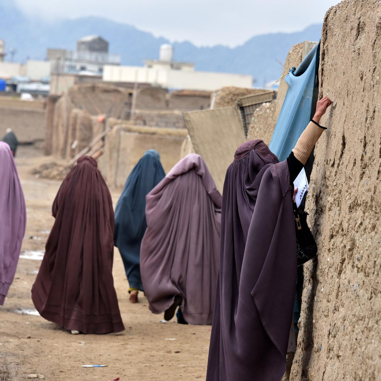 Women in lavender, blue, and burgundy burkas who are part of an immunization team write a message on the wall of a stone house during a vaccination campaign in Kandahar, Afghanistan on January 28, 2020. 