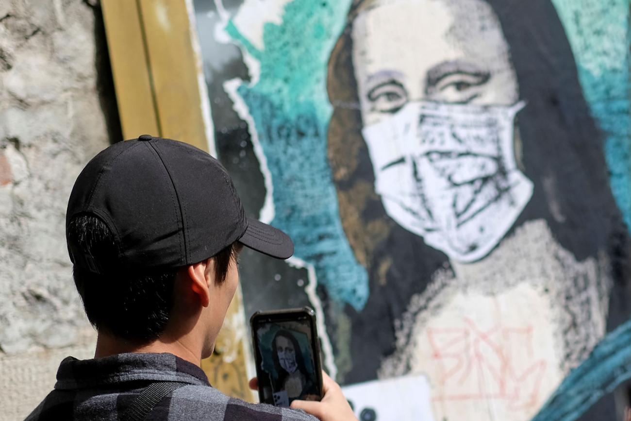 A tourist takes a picture of an image of Mona Lisa with a protective face mask after further cases of coronavirus were confirmed in Barcelona, Spain on March 6, 2020. The photo shows a man with dark hair and a black cap taking a cell phone photo of a likeness of Da Vinci's most famous painting with Mona wearing a mask. REUTERS/Nacho Doce