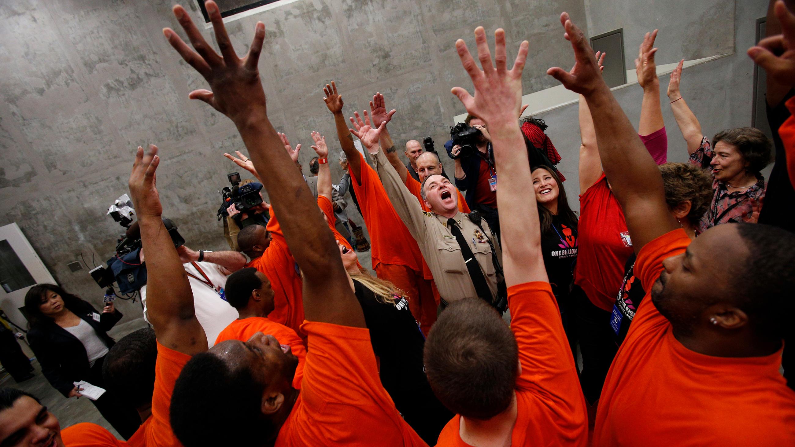 The photo shows a group of officers and inmates raising their hands in the air. 