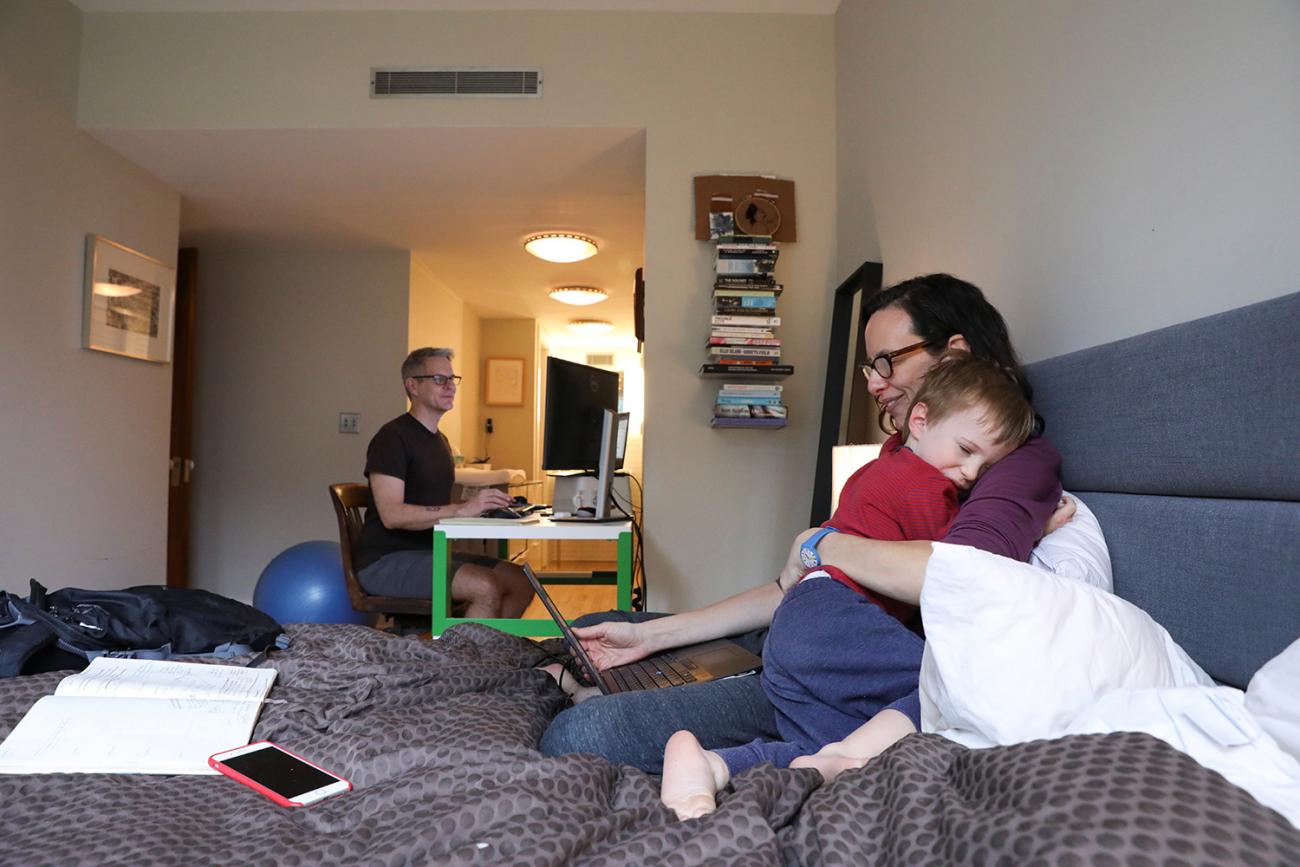 The photo shows her holding the child while reading off a device while her husband can be seen in the background on a computer. 