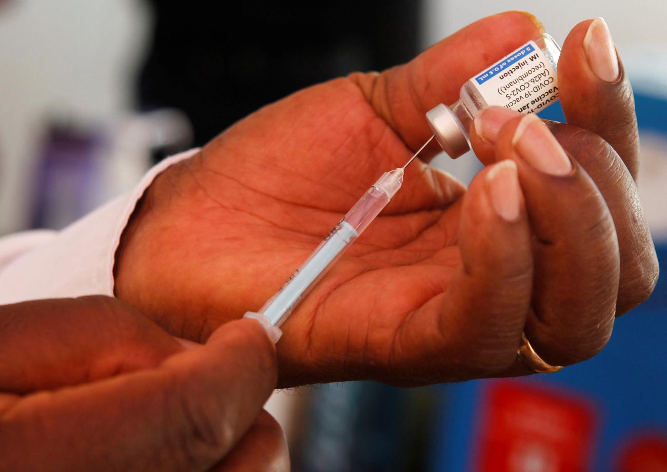 A hand holds a vial of the COVID-19 vaccine as a syringe is put into it to extract the product.
