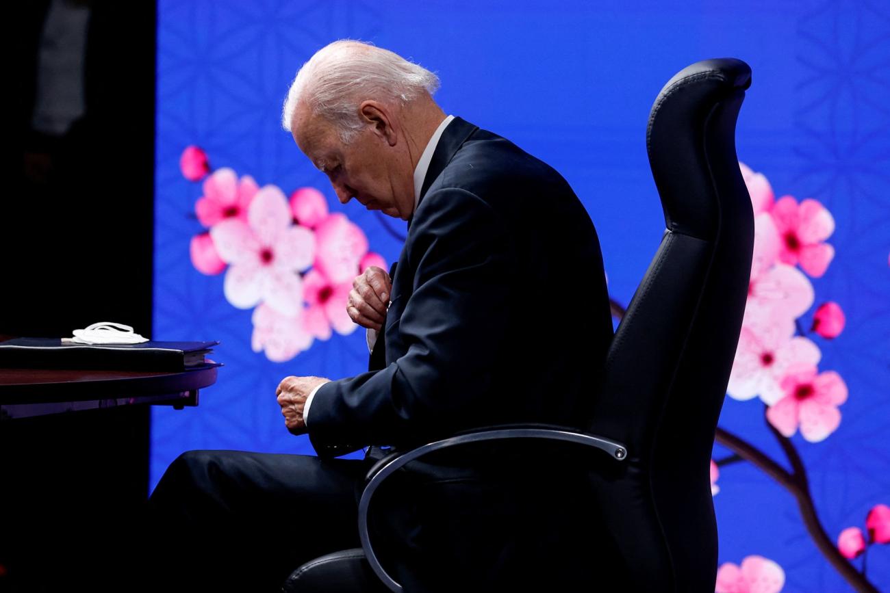 President Biden slouches over in a chair over a cherry blossom screen