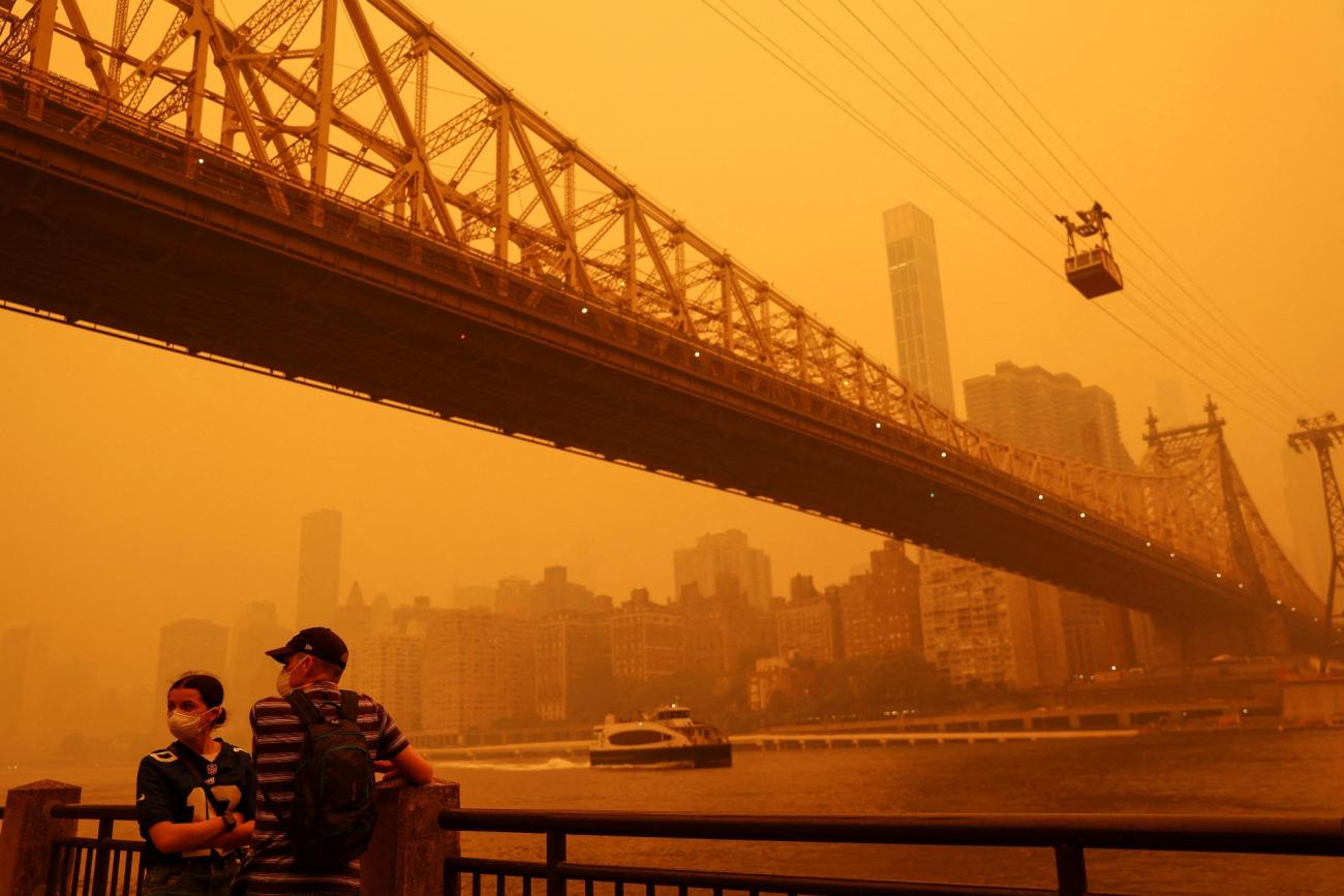 People wear protective masks as the Roosevelt Island Tram crosses the East River while haze and smoke from the Canadian wildfires shroud the Manhattan skyline in the Queens Borough New York City, U.S., June 7, 2023.People wear protective masks as the Roosevelt Island Tram crosses the East River while haze and smoke from Canadian wildfires shroud the Manhattan skyline, in Queens, New York City, on June 7, 2023. 