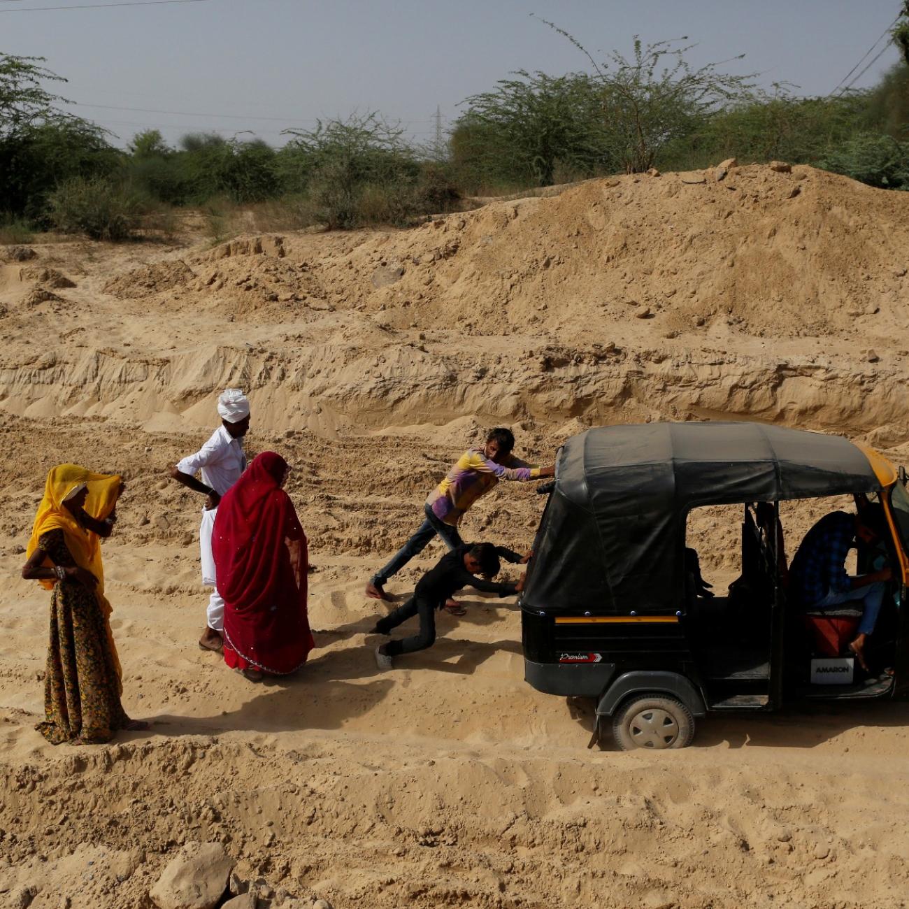 Bhawri Devi watches as her husband and son push an auto-rickshaw which got stuck in the sand on the way home from receiving cancer treatment, in a village in Jalore, India, on April 7, 2018. 