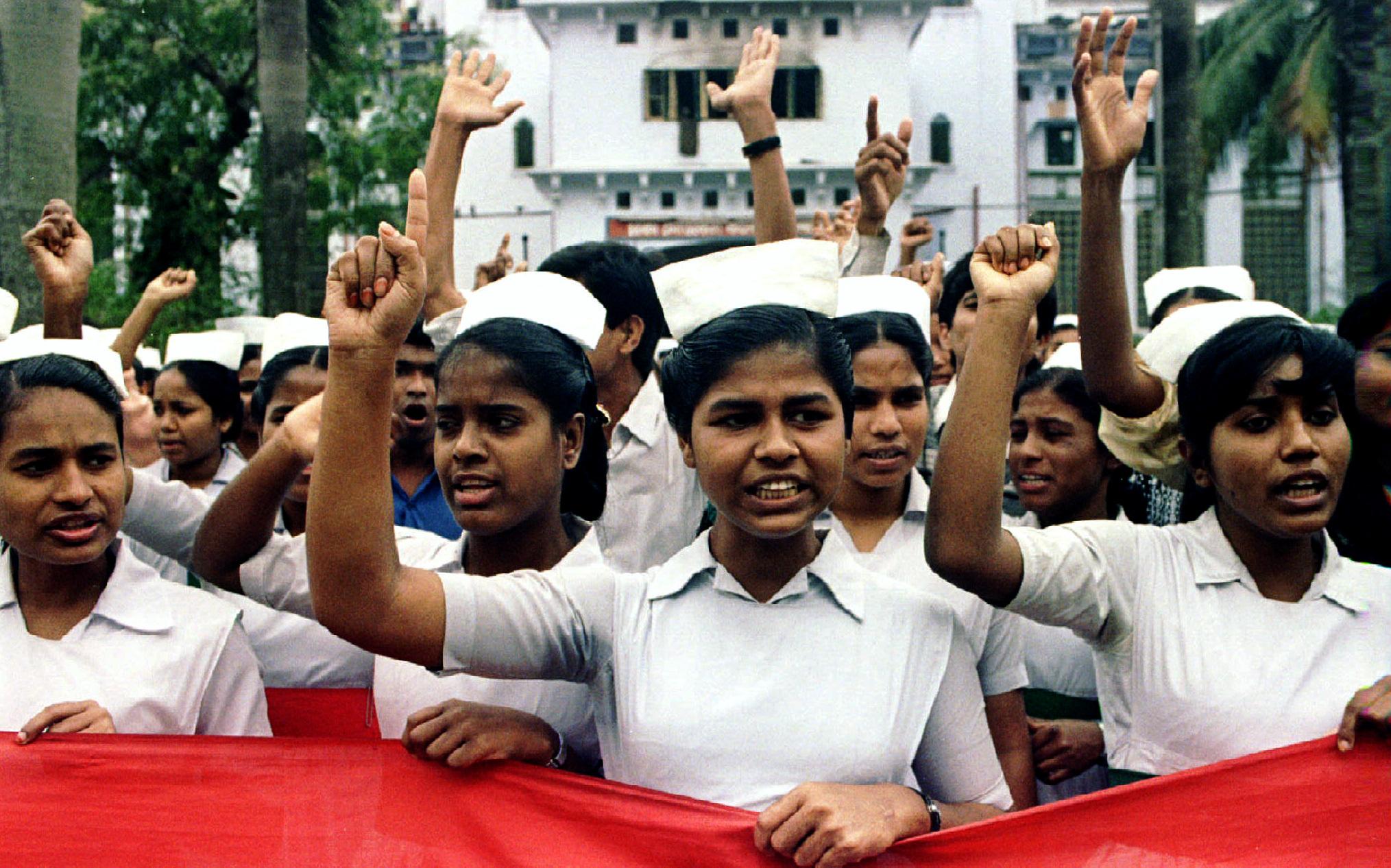 Nurses in white hats and uniforms raise their fists and hold a red banner in front of a white administration building in Dhaka, Bangladesh on February 16, 1995.