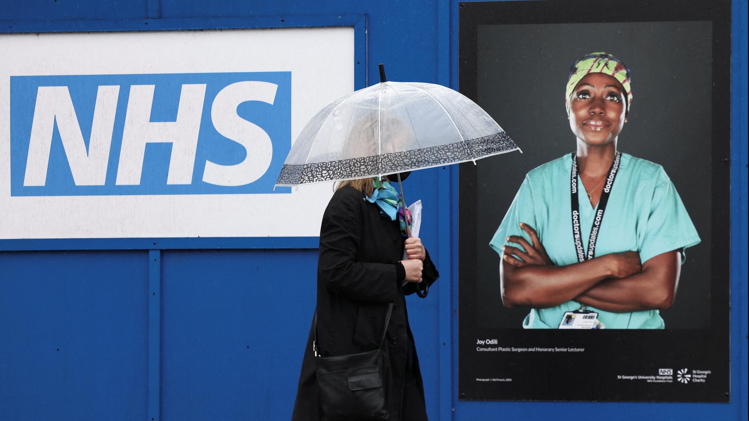 A woman walks past a poster of a NHS worker displayed on hoardings outside a temporary field hospital at St. George's Hospital, in London, Britain, on January 8, 2022