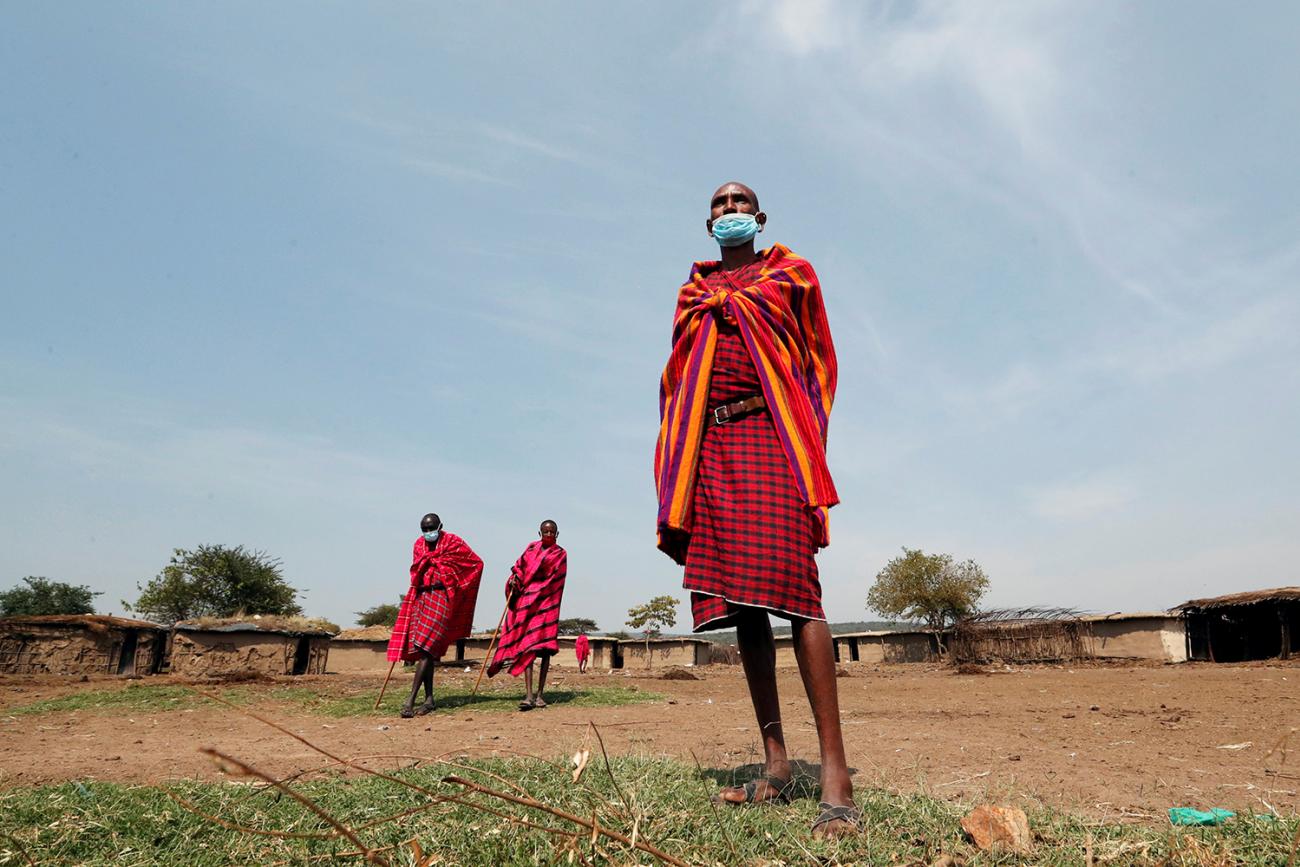 Maasai elders, wearing traditional clothes and facemasks due to coronavirus, gather within the Orboma Manyatta in Sekenani, near the Maasai Mara game reserve in Kenya, on August 10, 2020. This is a striking photo that shows a number of the elders in brightly colored reddish clothing on a clear day against a backdrop of what appears to be a village. REUTERS/Thomas Mukoya