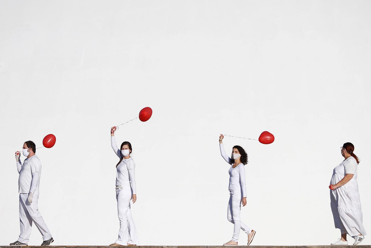 Artists perform with red balloons at a protest in honor of people who died from coronavirus disease (COVID-19) during its outbreak in Brasilia, Brazil, on June 1, 2020. The photo shows four artists dressed in white walking in front of a massive white backdrop. Each holds a red balloon. REUTERS/Adriano Machado
