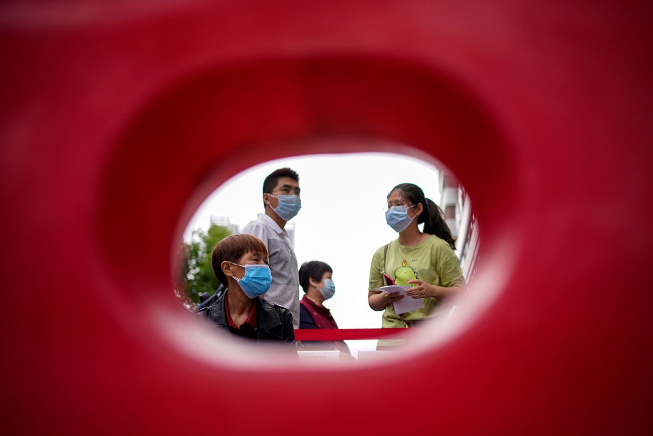Residents wearing face masks queue for nucleic acid testings in Wuhan, the Chinese city hit hardest by the coronavirus disease (COVID-19) outbreak, Hubei province, China May 16, 2020. The photo shows what appears to be a family through the hole of a plastic barricade. REUTERS/Aly Song