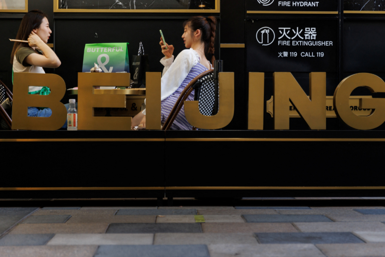 Two women relax in a cafe behind a sign with large letters spelling out Beijing, in a shopping area in Beijing, China, on July 14, 2022. 